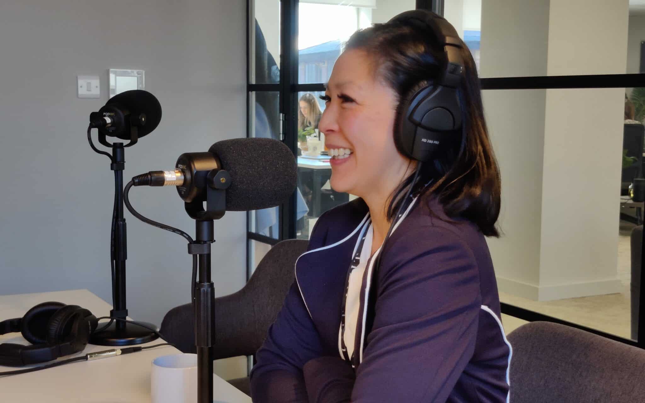 A close-up of a podcast participant wearing headphones and speaking into a microphone at Innobella Media's pop-up podcast recording studio setup in the boardroom of Unit Chambers' city centre offices in Liverpool.